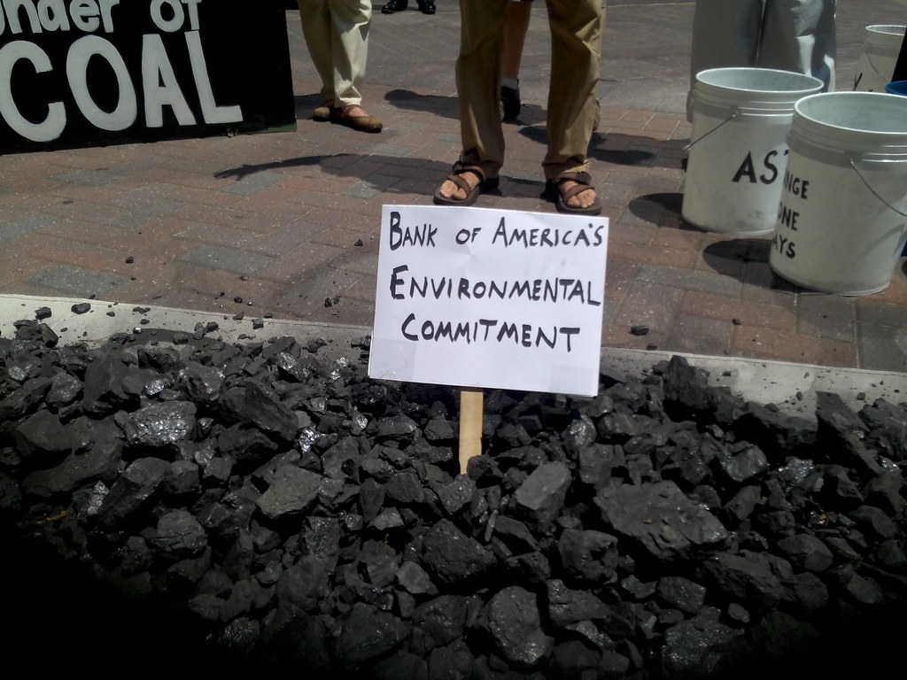 Bank of America's Environmental Commitment on a white sign stuck in a pile of burnt coal