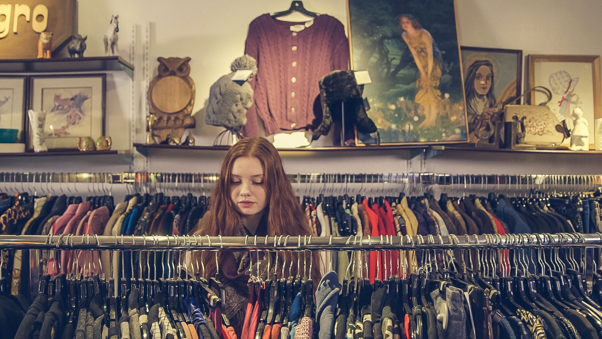 Redhead girl browsing a clothing rack at a thrift store